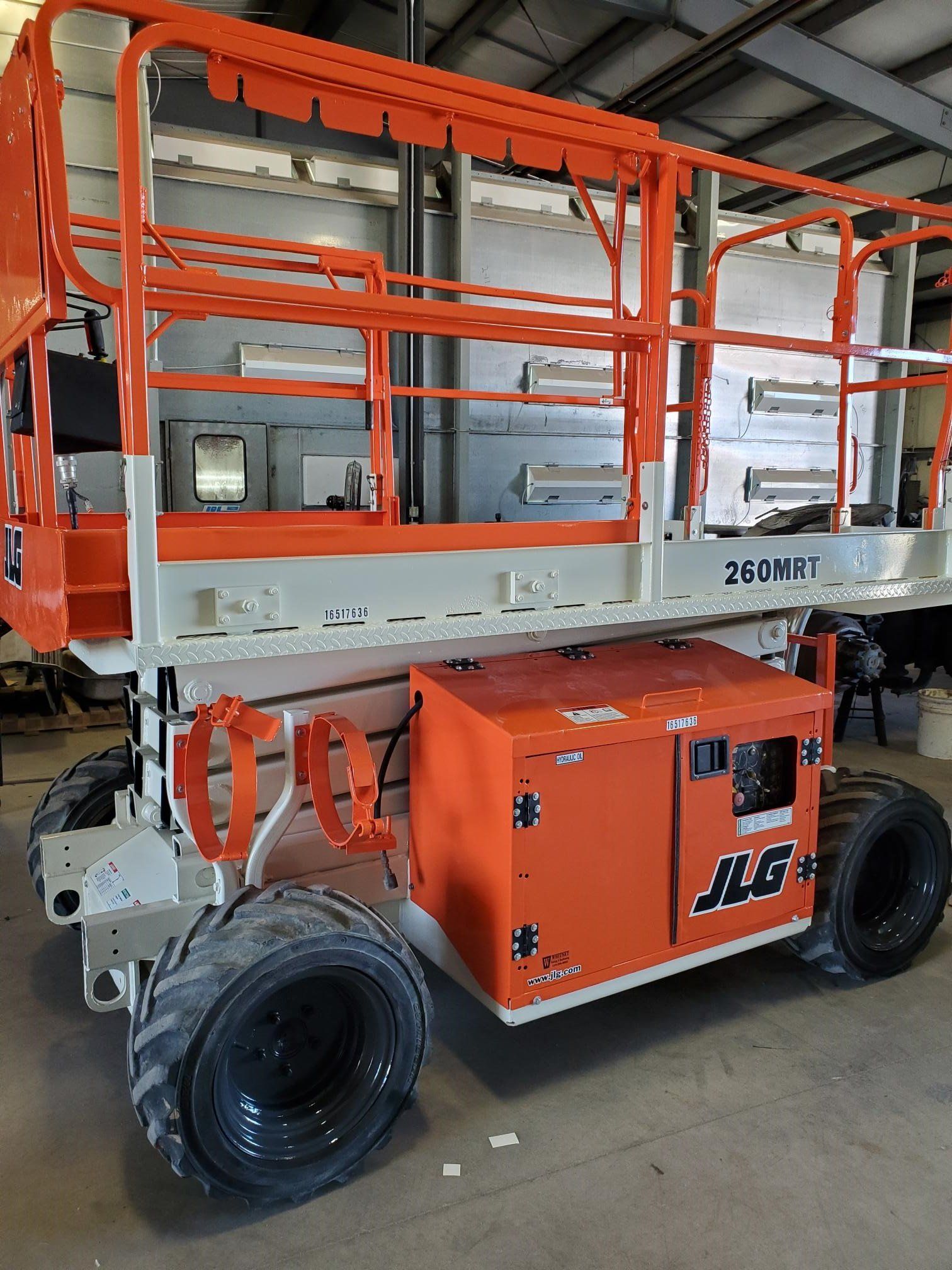 Orange and white JLG aerial lift platform with large tires, in a workshop.