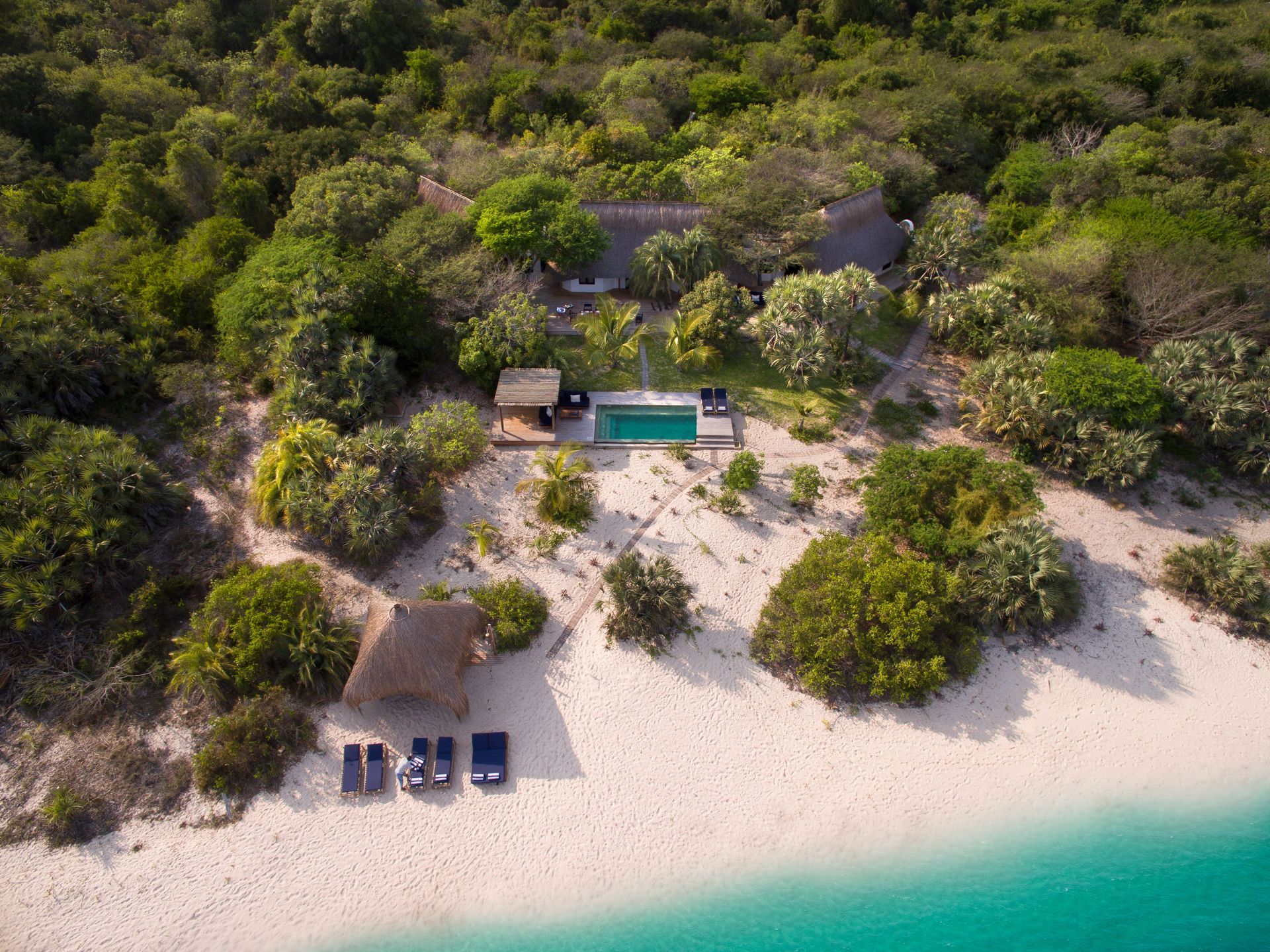 An aerial view of a tropical beach with a swimming pool surrounded by trees.