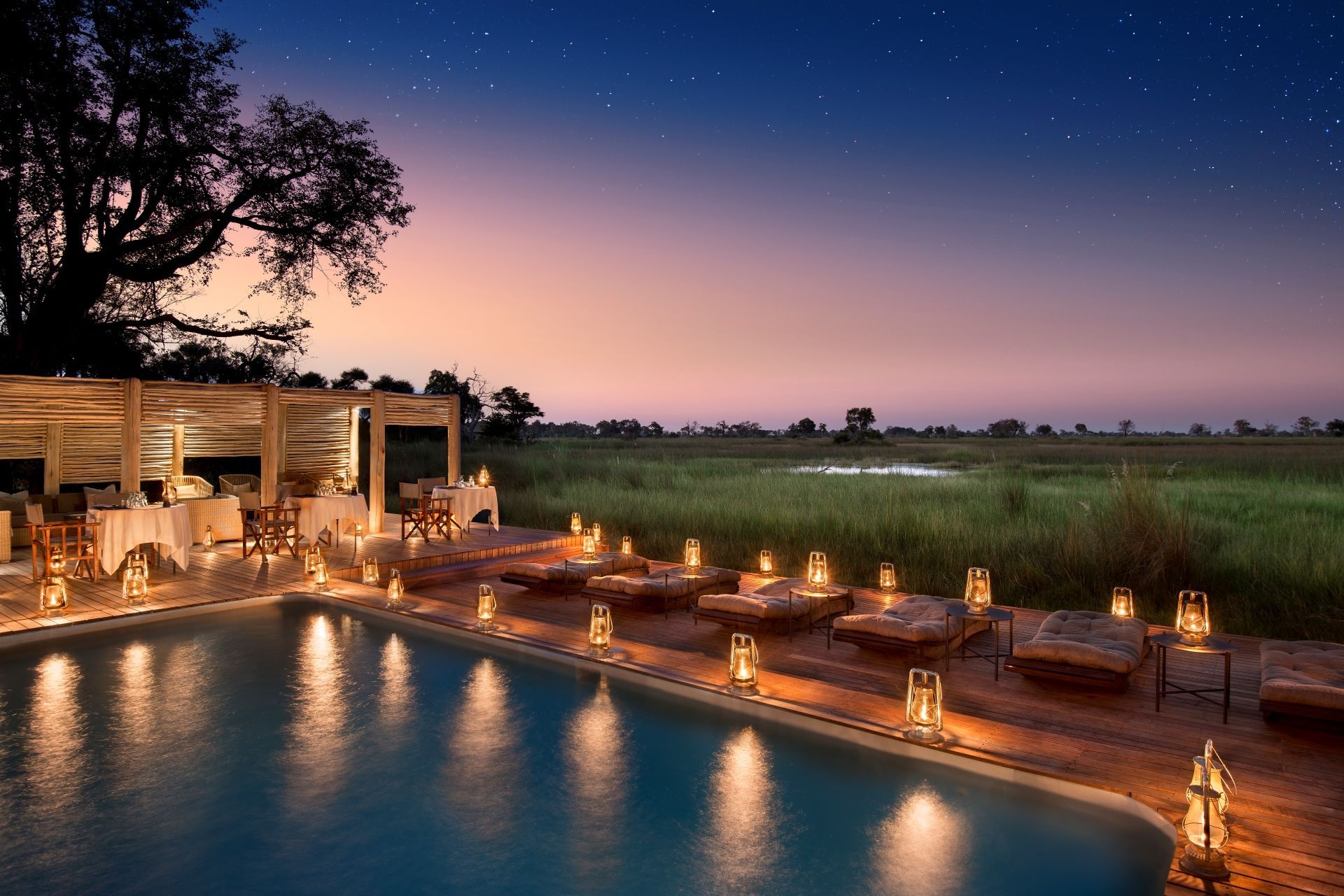 A swimming pool surrounded by candles and chairs at night