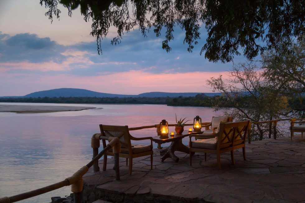 A sunset over a lake with a table and chairs