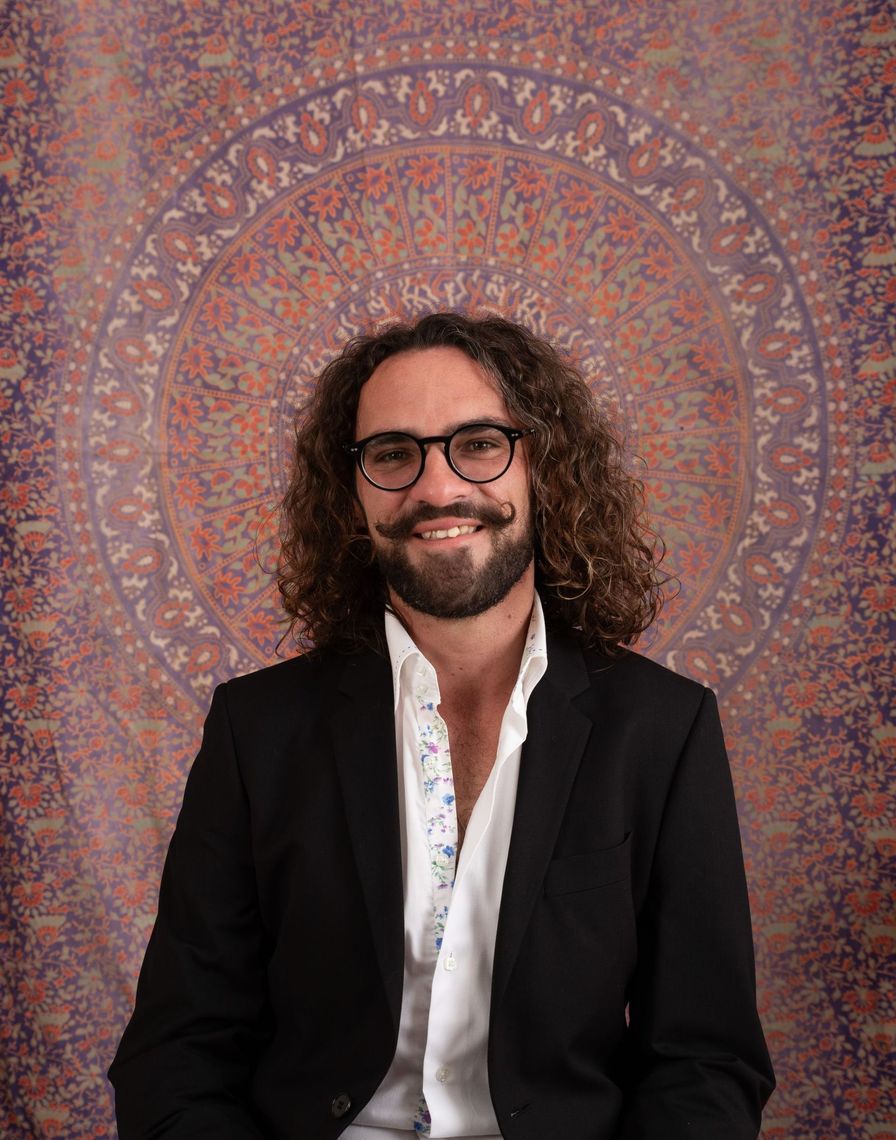 A man with curly hair and glasses is wearing a black jacket and a white shirt.