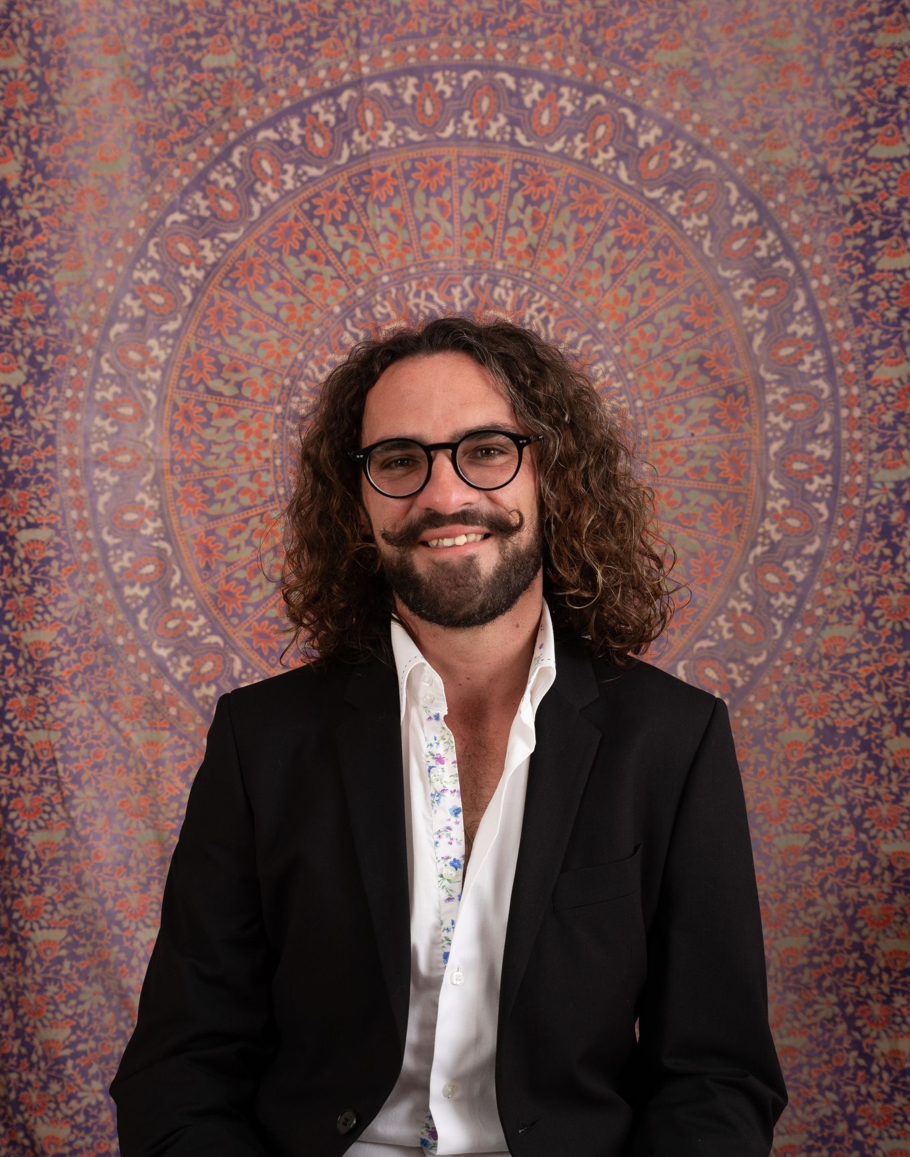A man with curly hair and glasses is wearing a black jacket and a white shirt.
