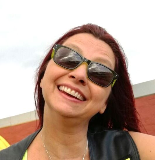 A woman wearing sunglasses is smiling and looking at the camera