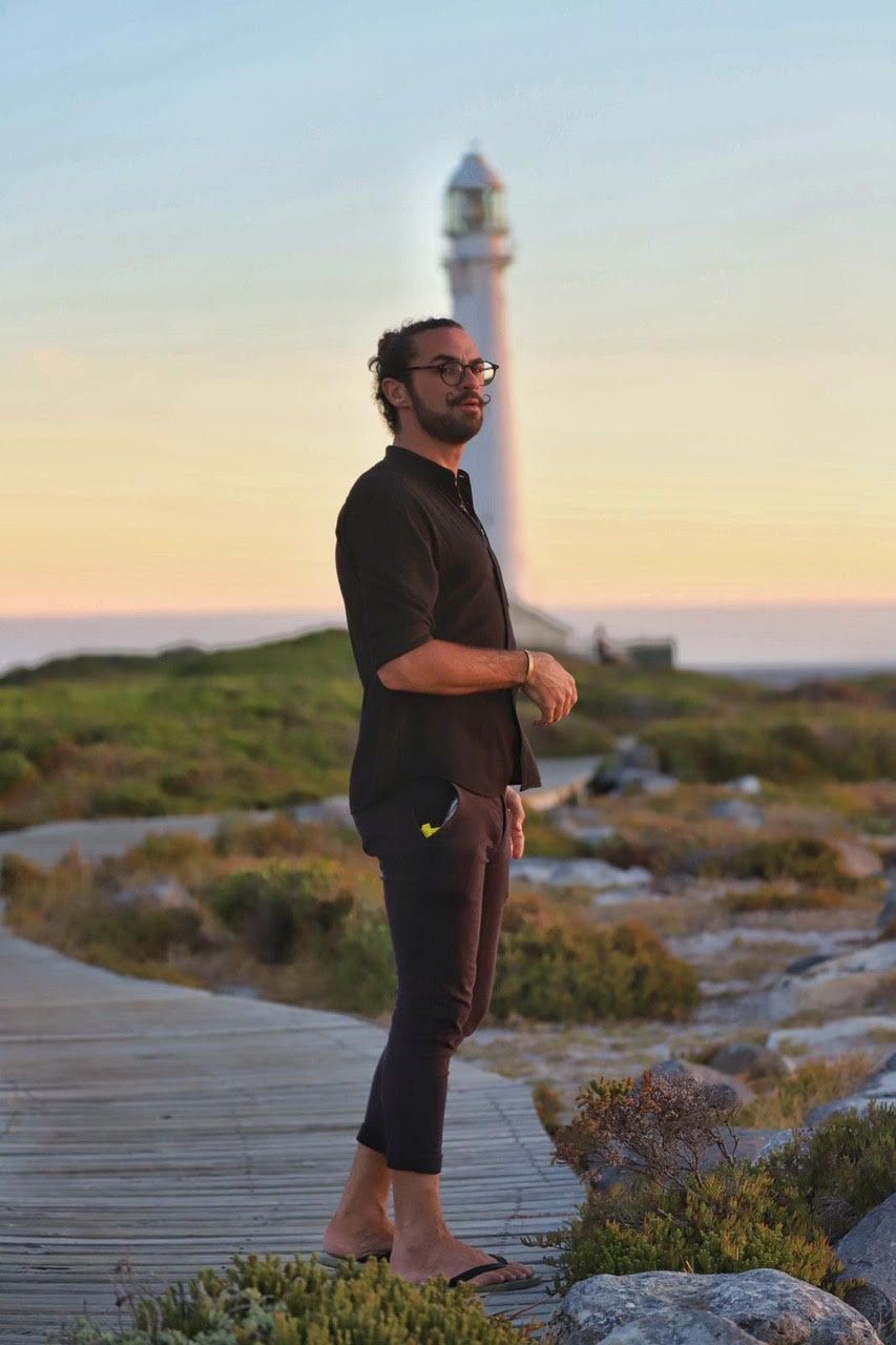 A man is standing on a wooden walkway in front of a lighthouse.