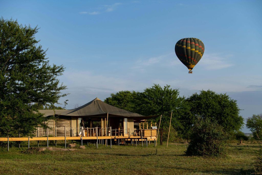 A hot air balloon is flying over a house in the middle of a field.
