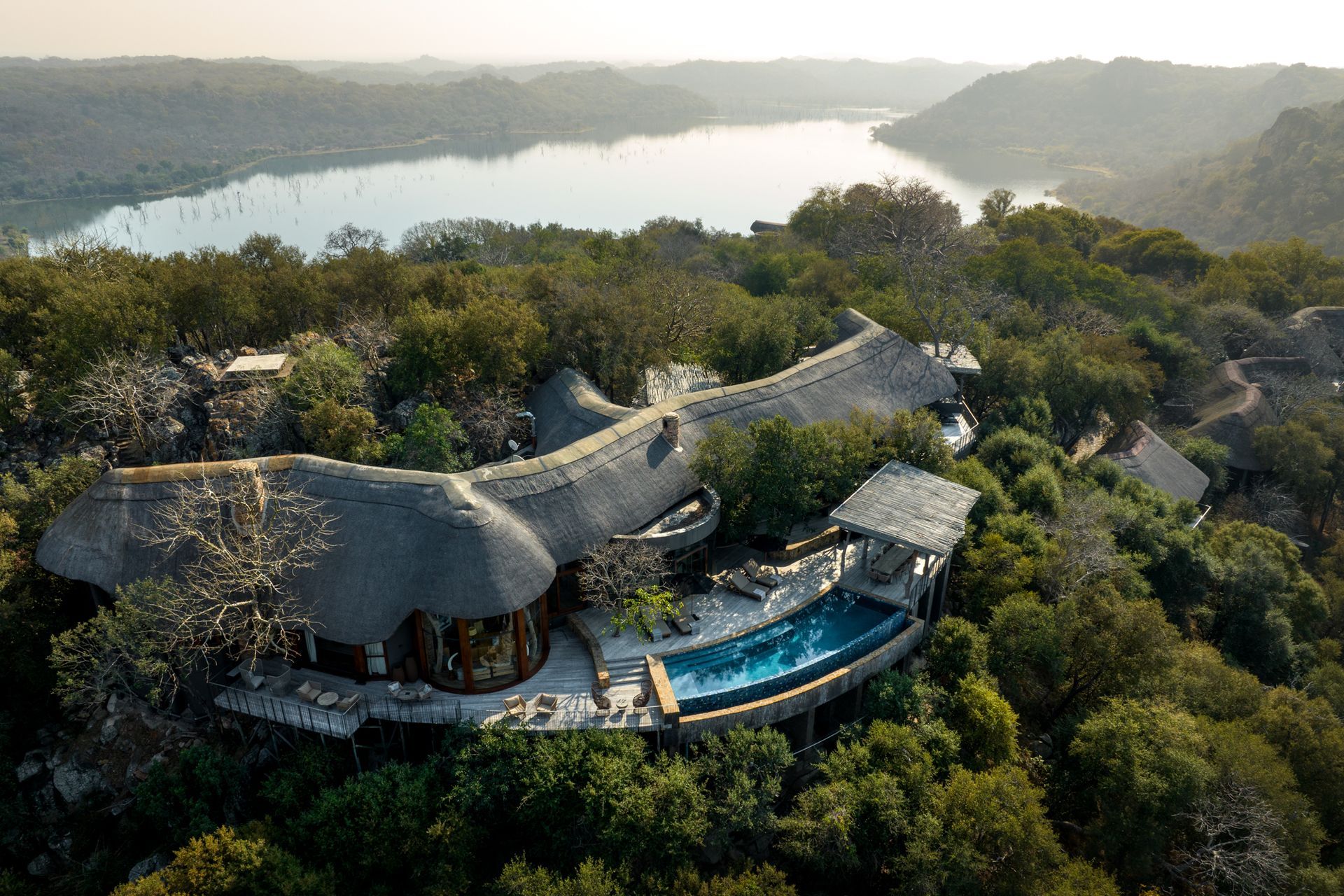 A large house with a green roof is surrounded by trees and rocks.