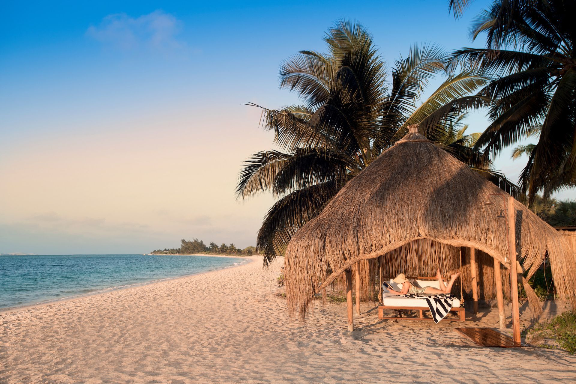 A thatched hut sits on a sandy beach near the ocean.