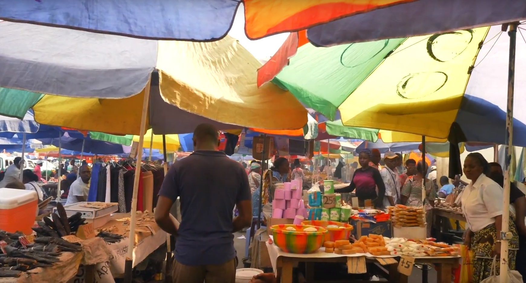 A man stands in a crowded market surrounded by colorful umbrellas
