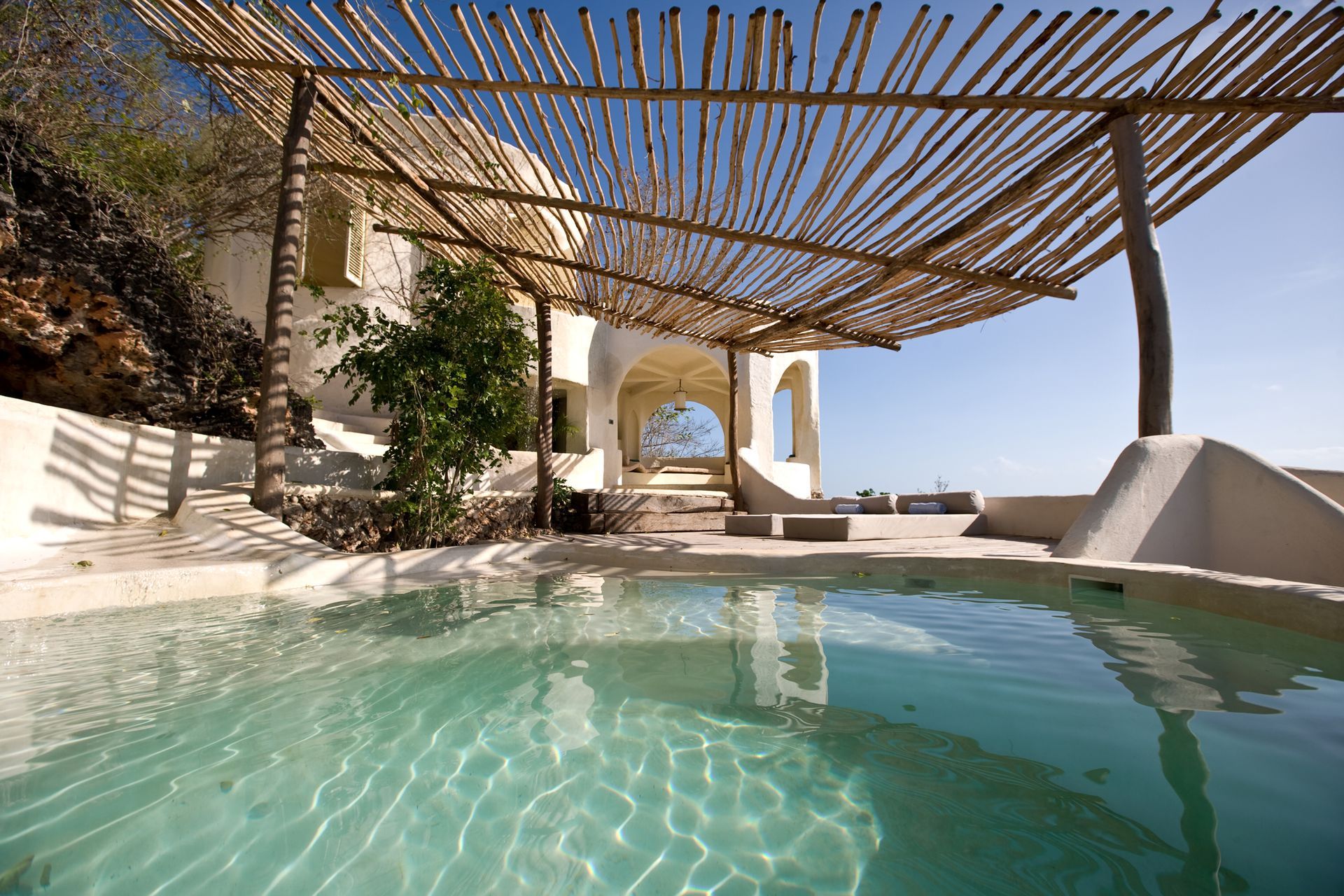 A swimming pool under a pergola with a house in the background