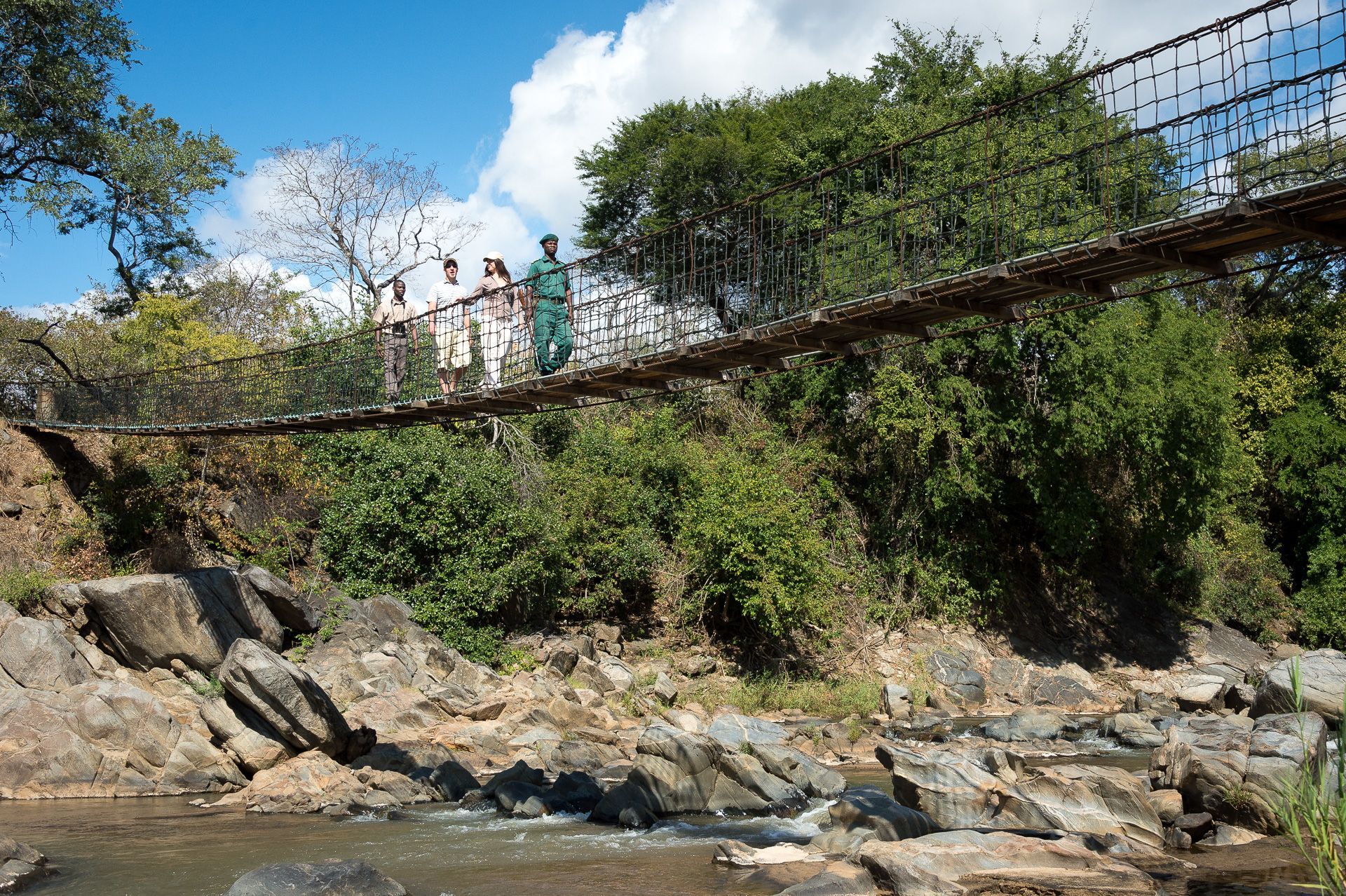A group of people are walking across a suspension bridge over a river.