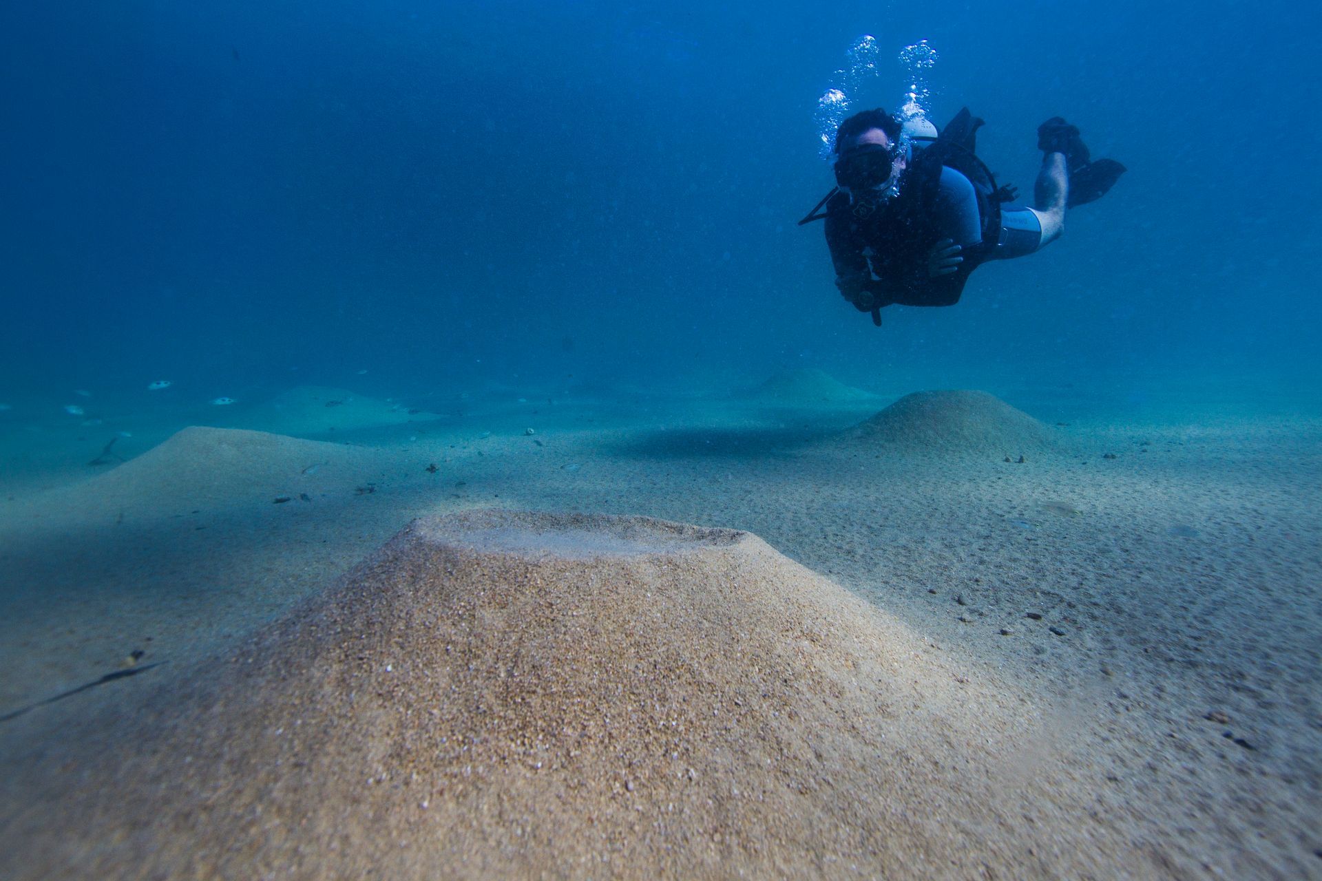A scuba diver is swimming in the ocean near a pile of sand.