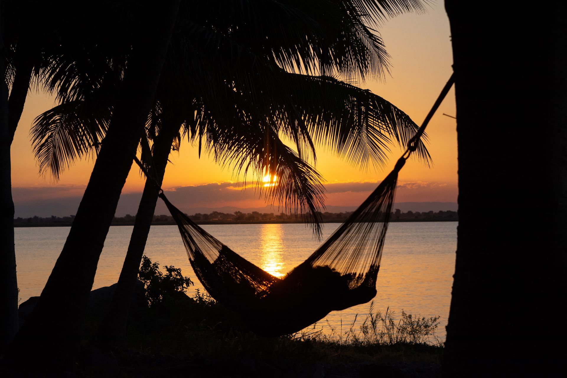 A person is laying in a hammock overlooking a body of water at sunset