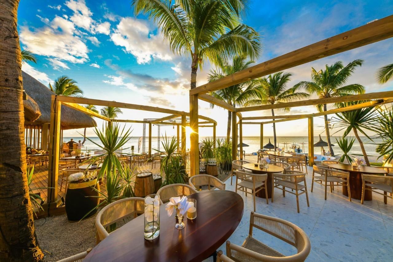 A restaurant with tables and chairs on the beach with palm trees in the background.