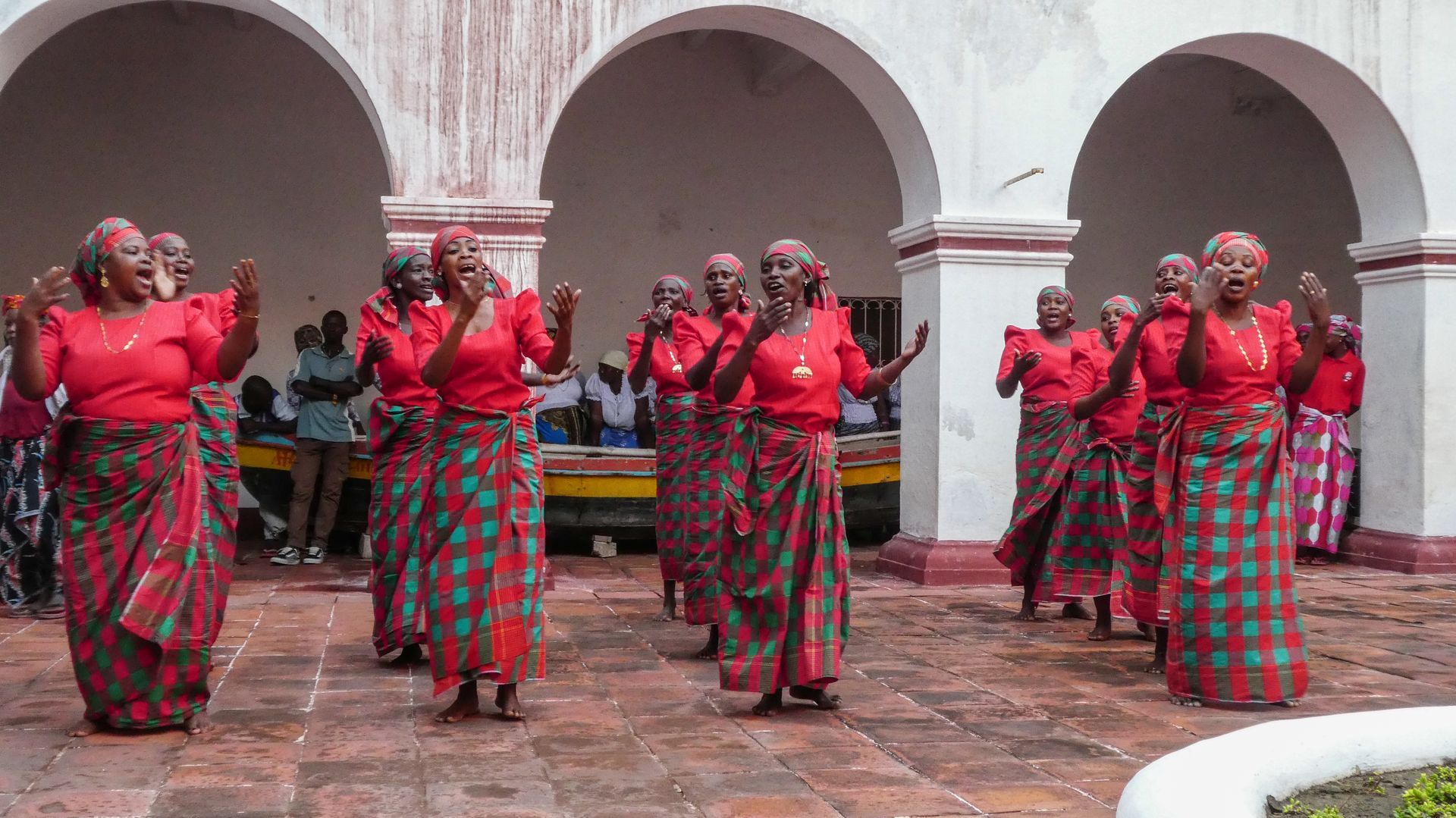 A group of women in red and green plaid skirts are dancing in a courtyard.