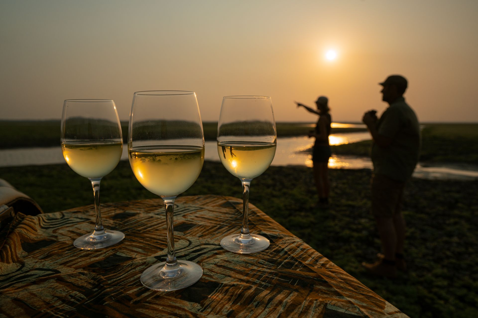 Three wine glasses are sitting on a table in front of a sunset.