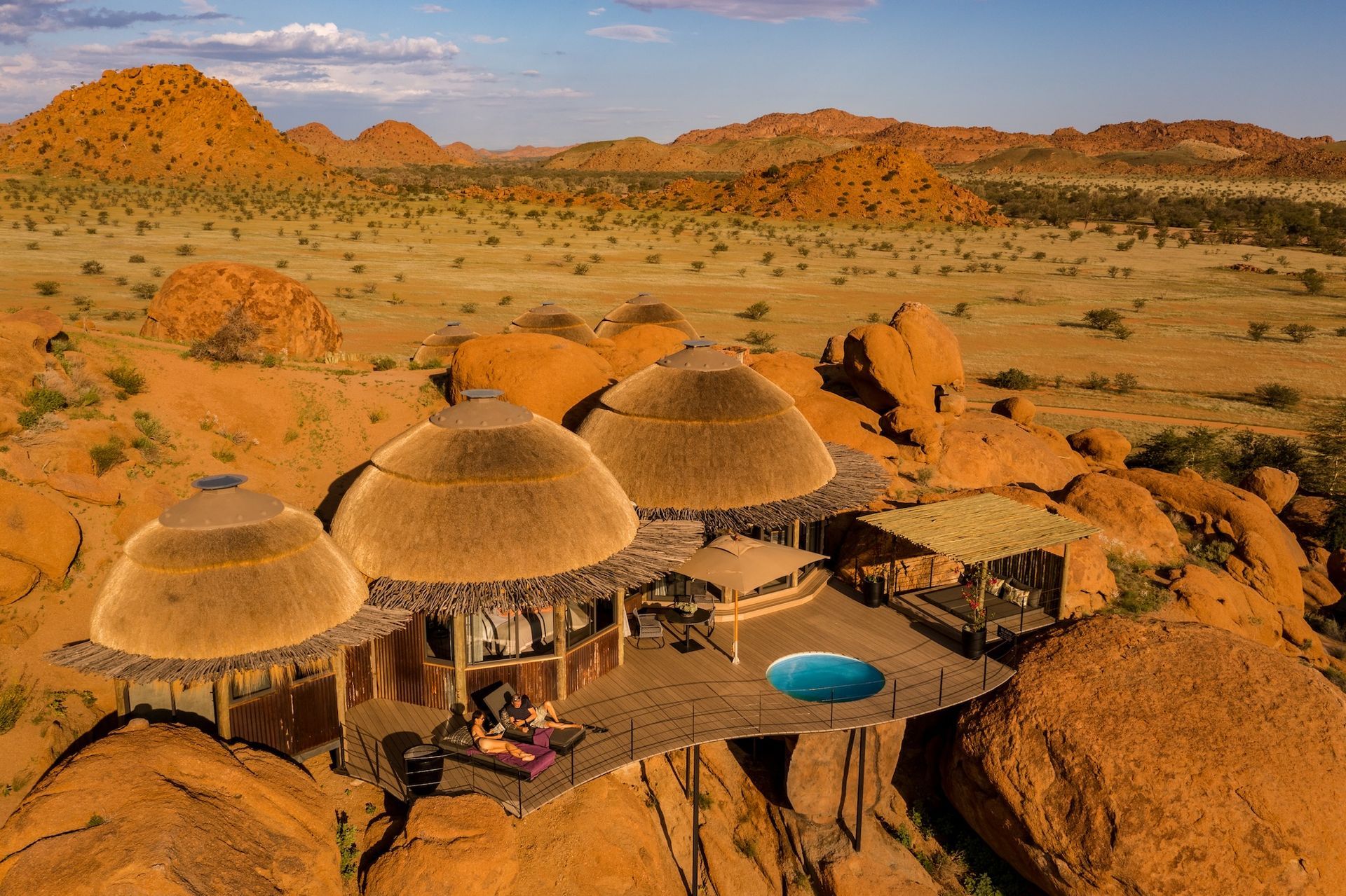 An aerial view of a thatched hut with a pool in the middle of the desert.