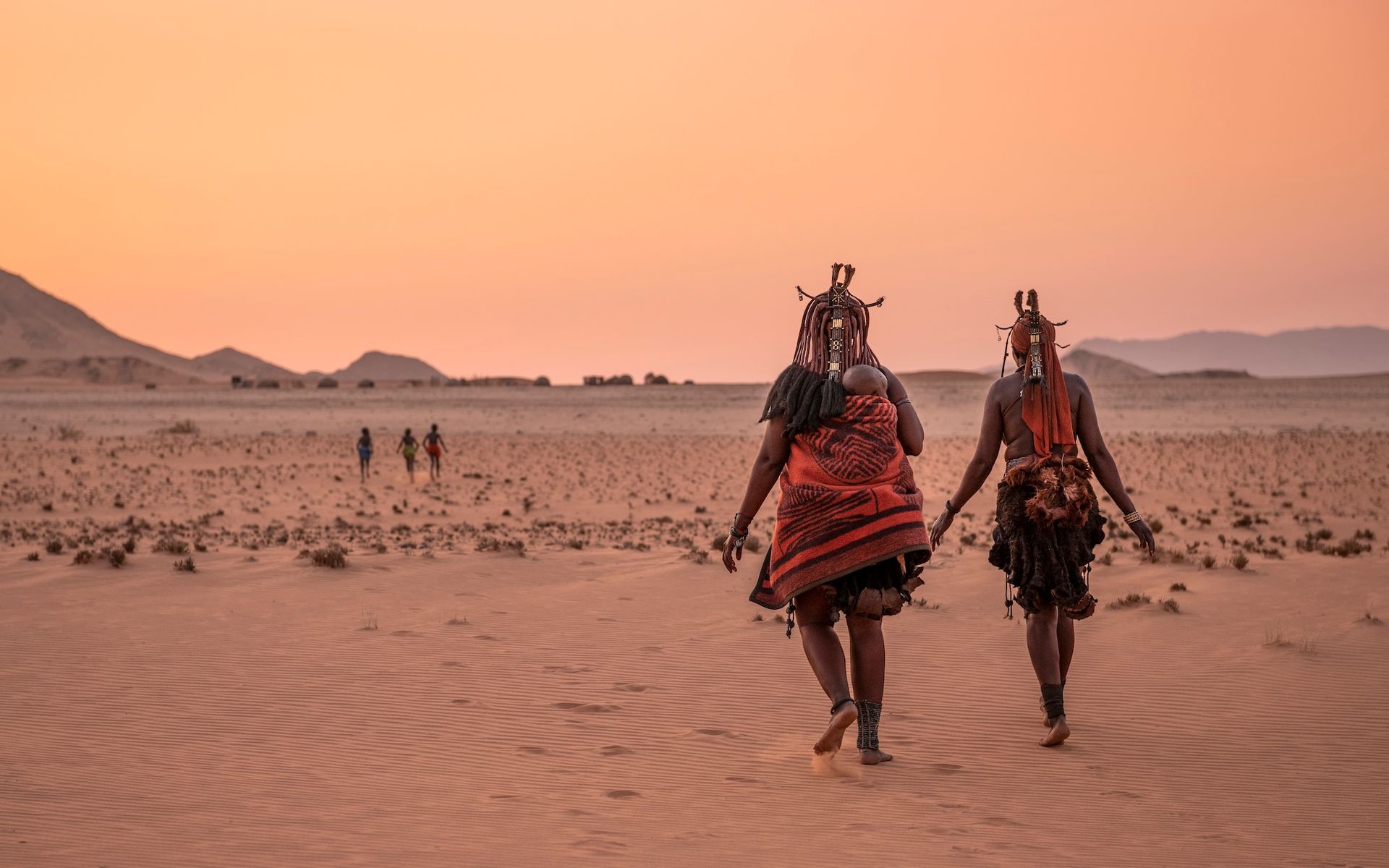 Two people are walking in the desert holding hands.