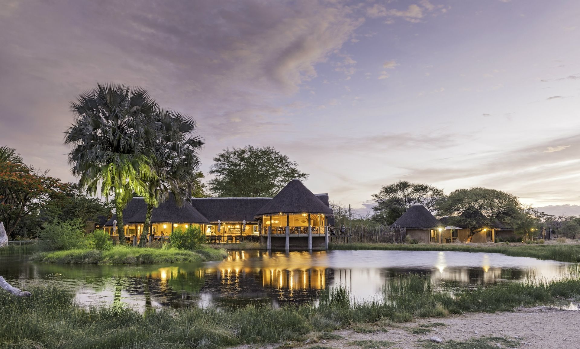 A large house is surrounded by trees and a pond.