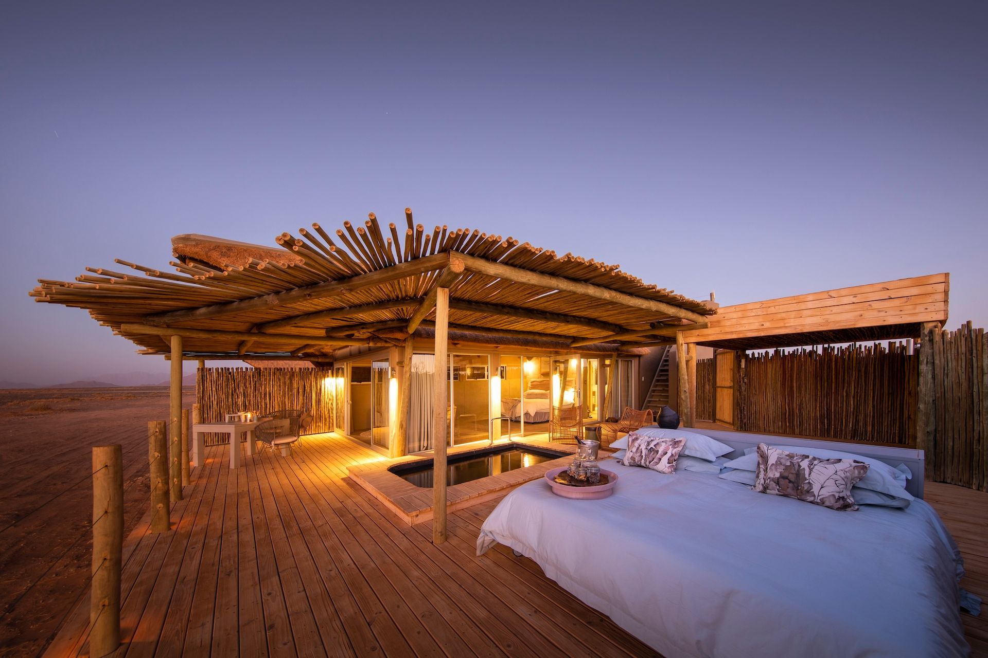 A bed is sitting on a wooden deck in front of a house.