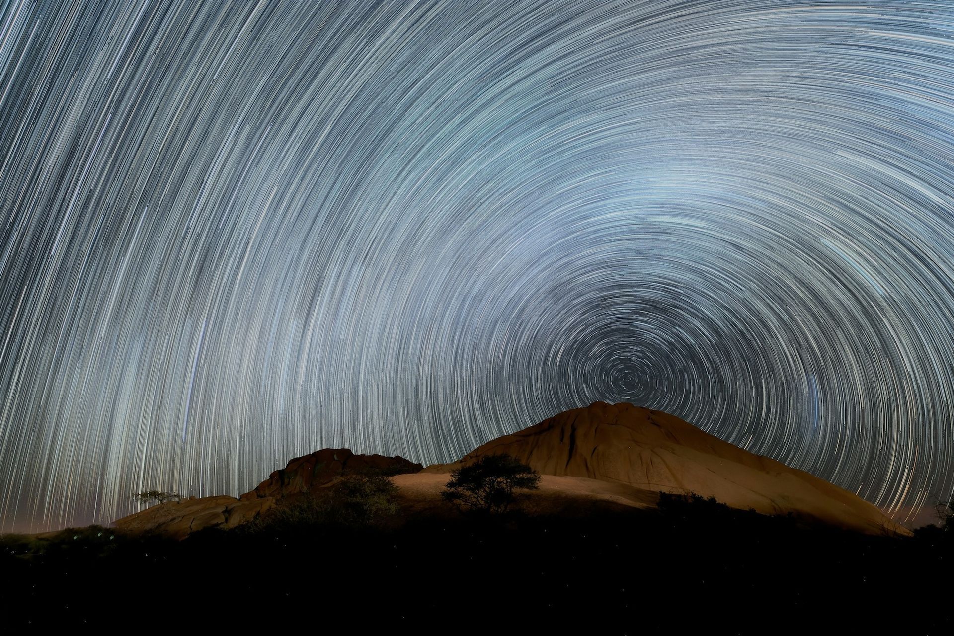A silhouette of a mountain against a starry sky at night.