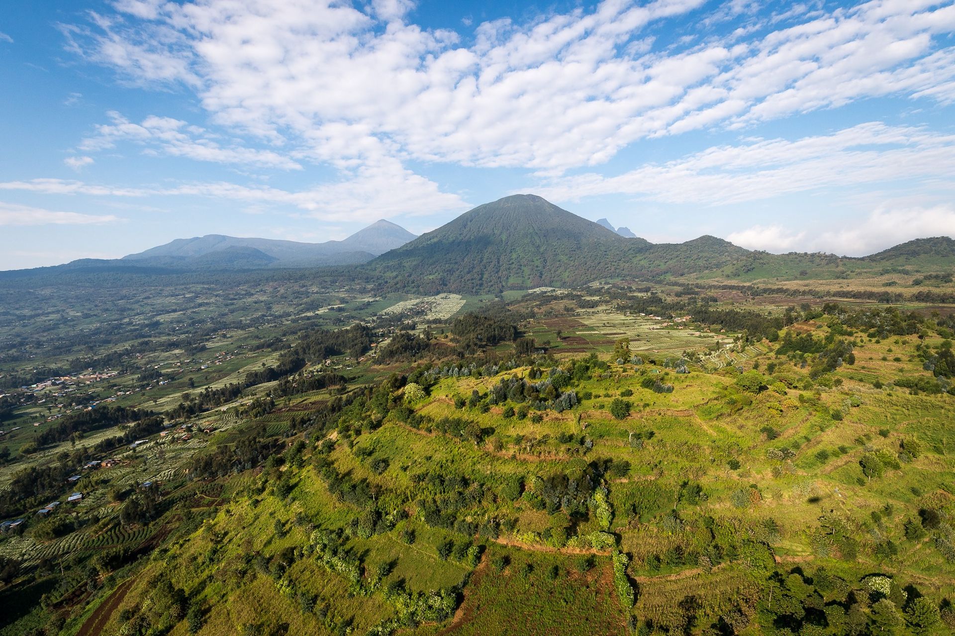 An aerial view of a lush green valley with mountains in the background.