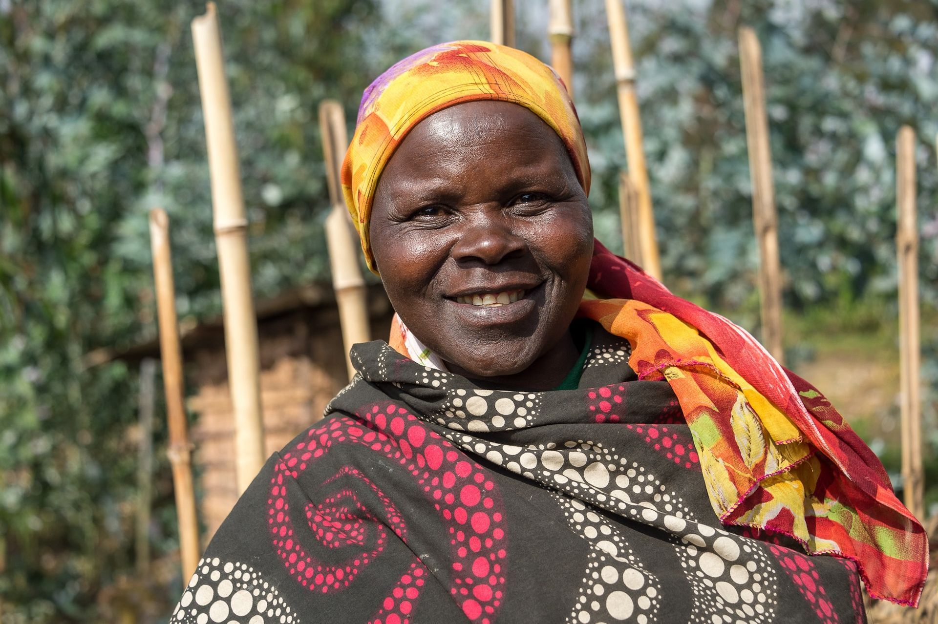 A woman wearing a head scarf and a blanket is smiling for the camera.