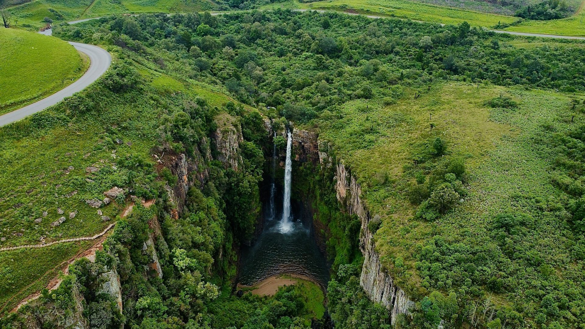 An aerial view of a waterfall surrounded by trees and a road.