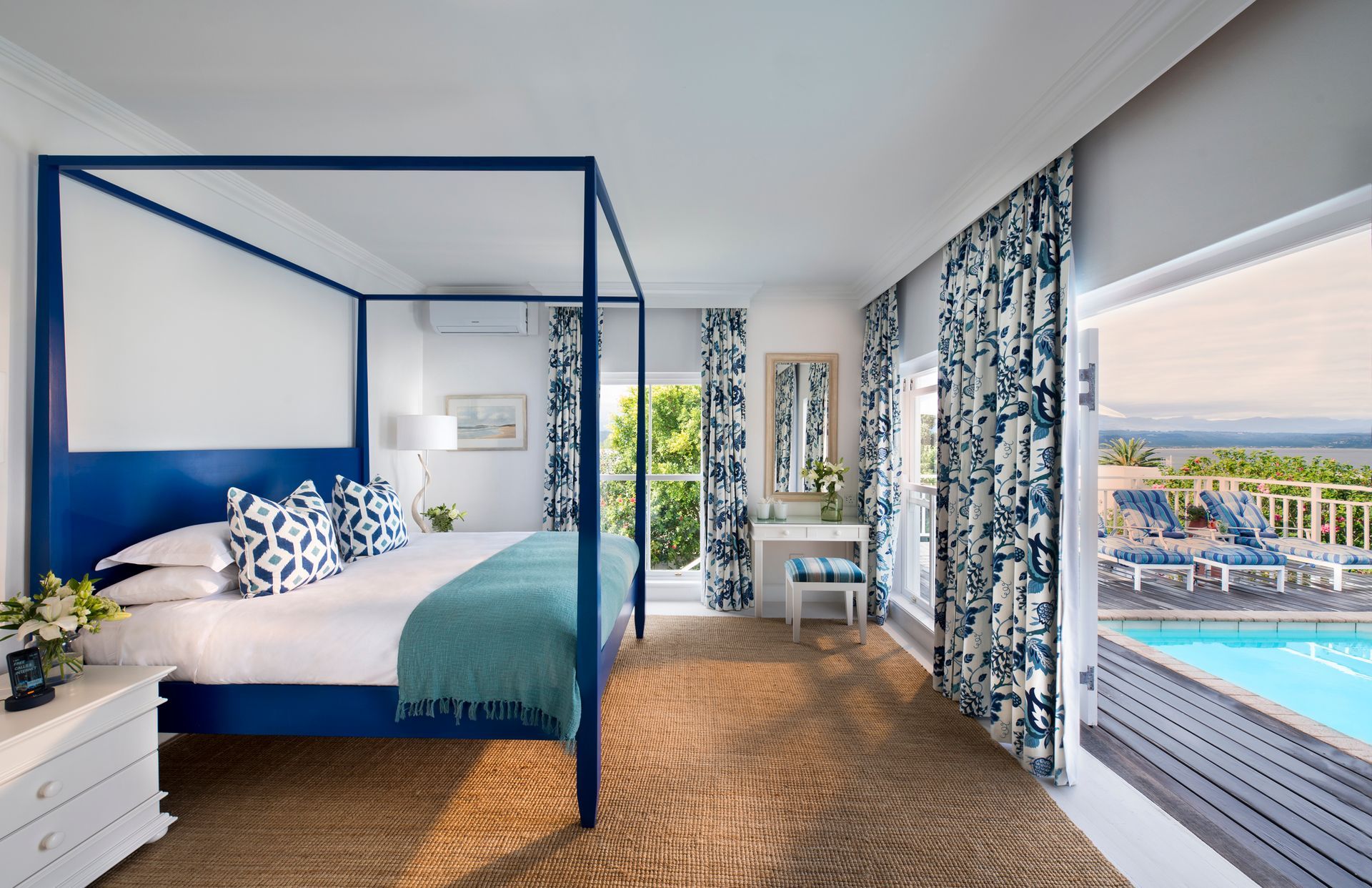 A bedroom with a blue canopy bed and a swimming pool in the background