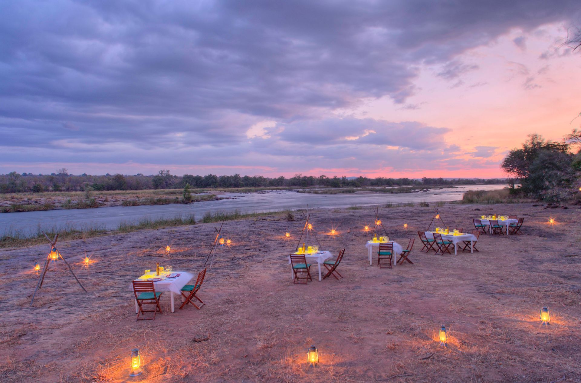 A group of tables and chairs are set up in the middle of a field next to a river.