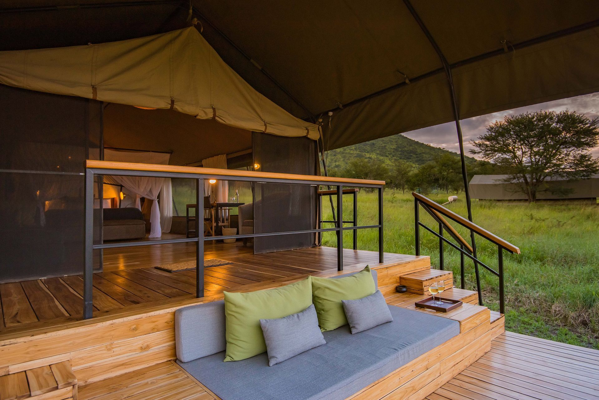 A wooden deck with a couch and pillows in front of a tent.