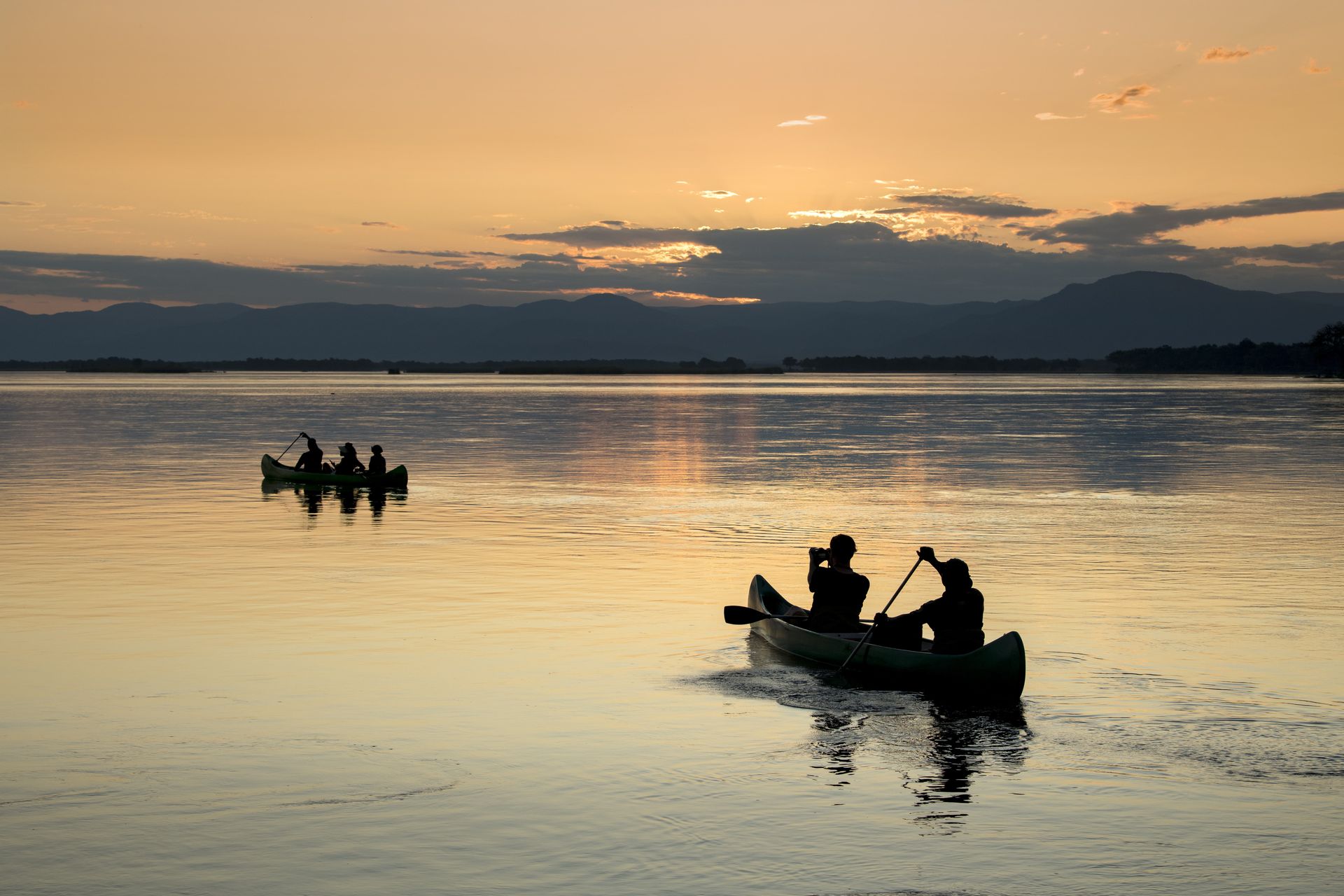 A group of people are in a canoe on a lake at sunset.