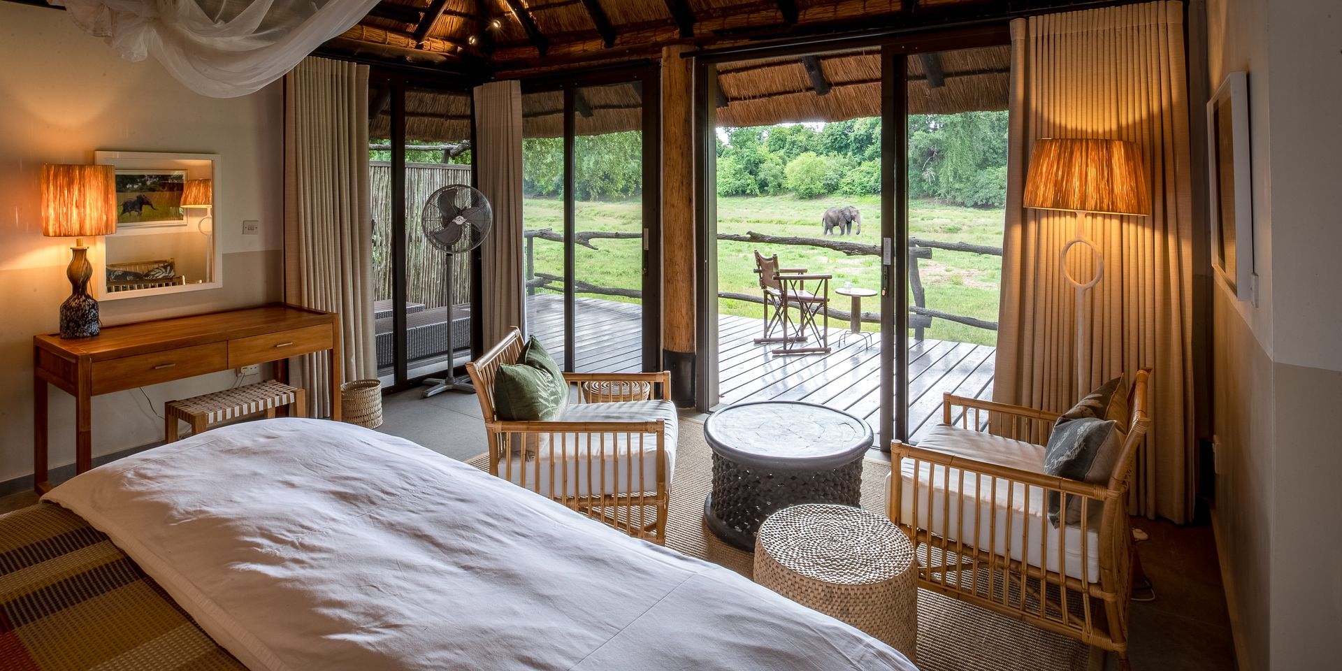 A bedroom with a bed , chairs , table and sliding glass doors leading to a deck.