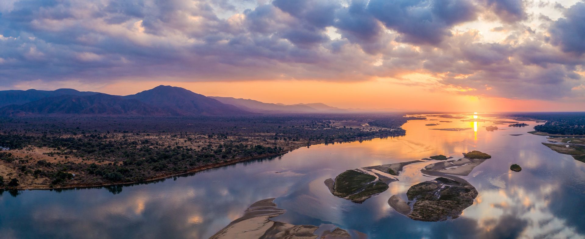 An aerial view of a river at sunset with mountains in the background.