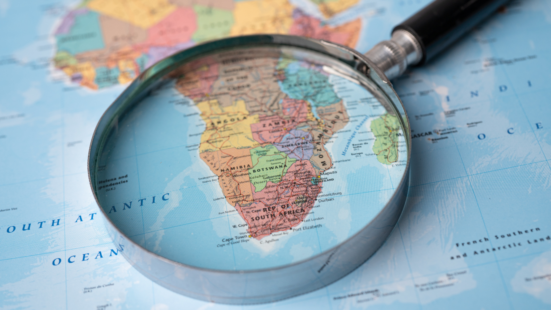 A magnifying glass positioned over a colorful map of Southern Africa, resting on a flat map background.