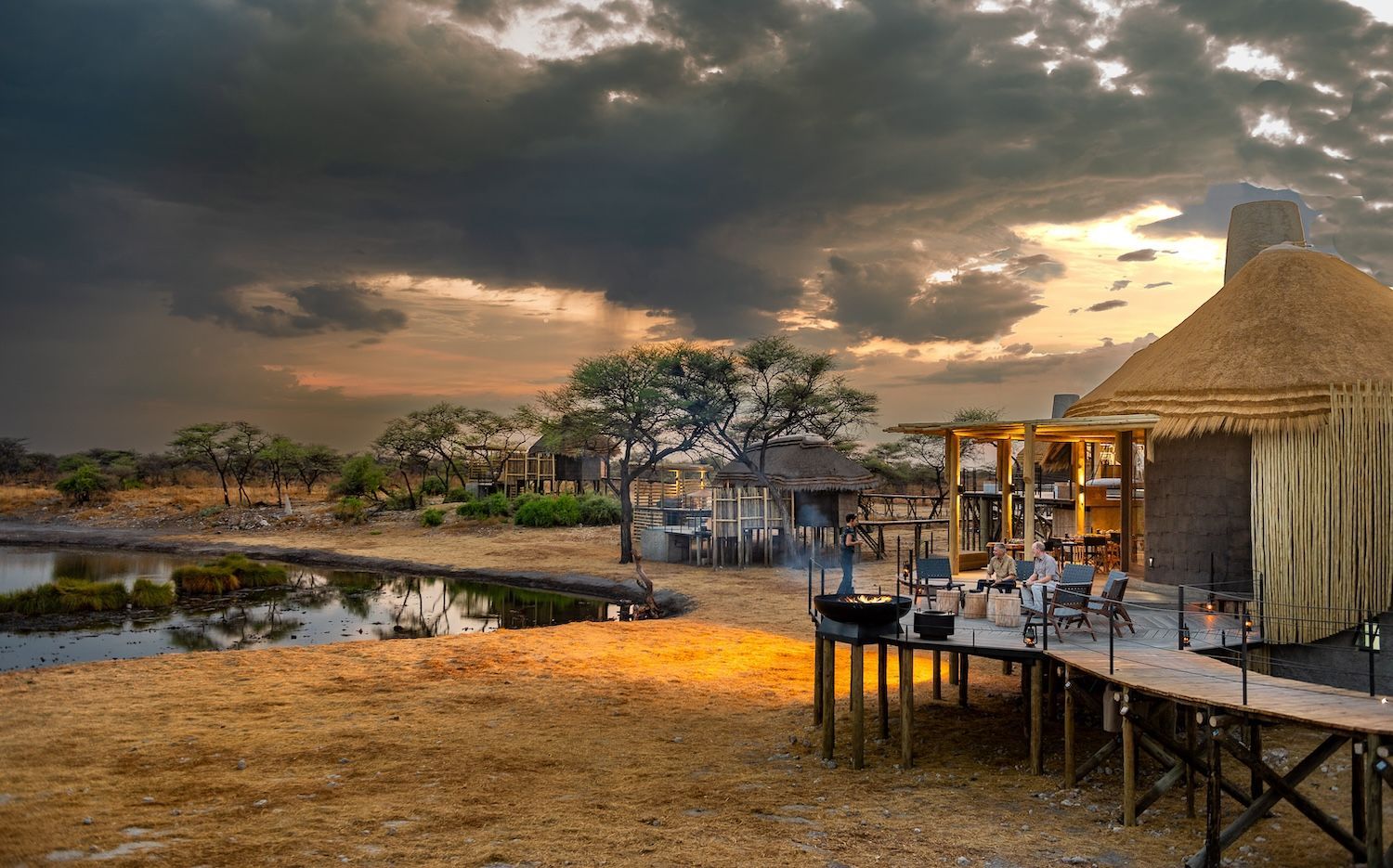 A hut with a thatched roof is sitting next to a body of water.