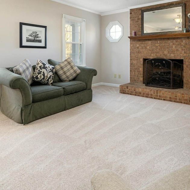 A living room with a green sofa, brick fireplace, and light beige carpet.