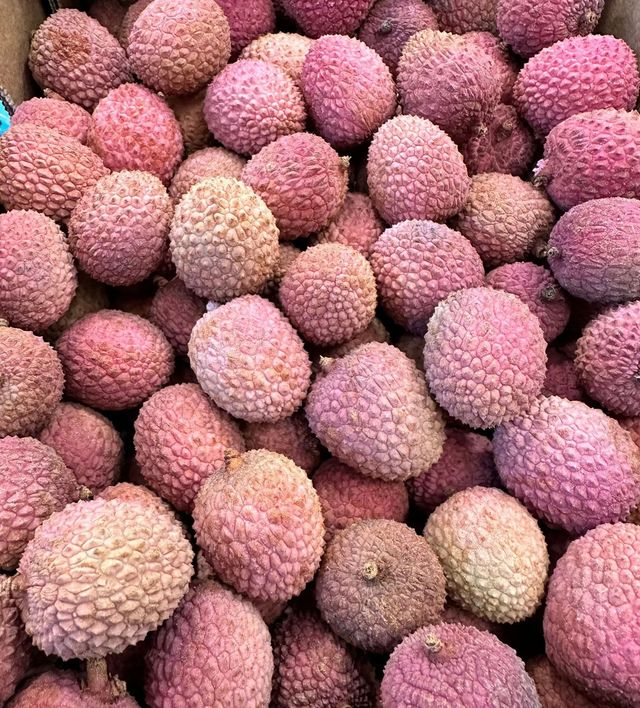 A pile of pink lychee fruits with rough, bumpy skins stacked tightly together