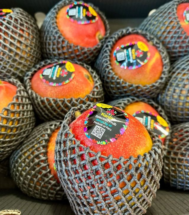 Netted mangoes with red-orange skins stacked together in a market display