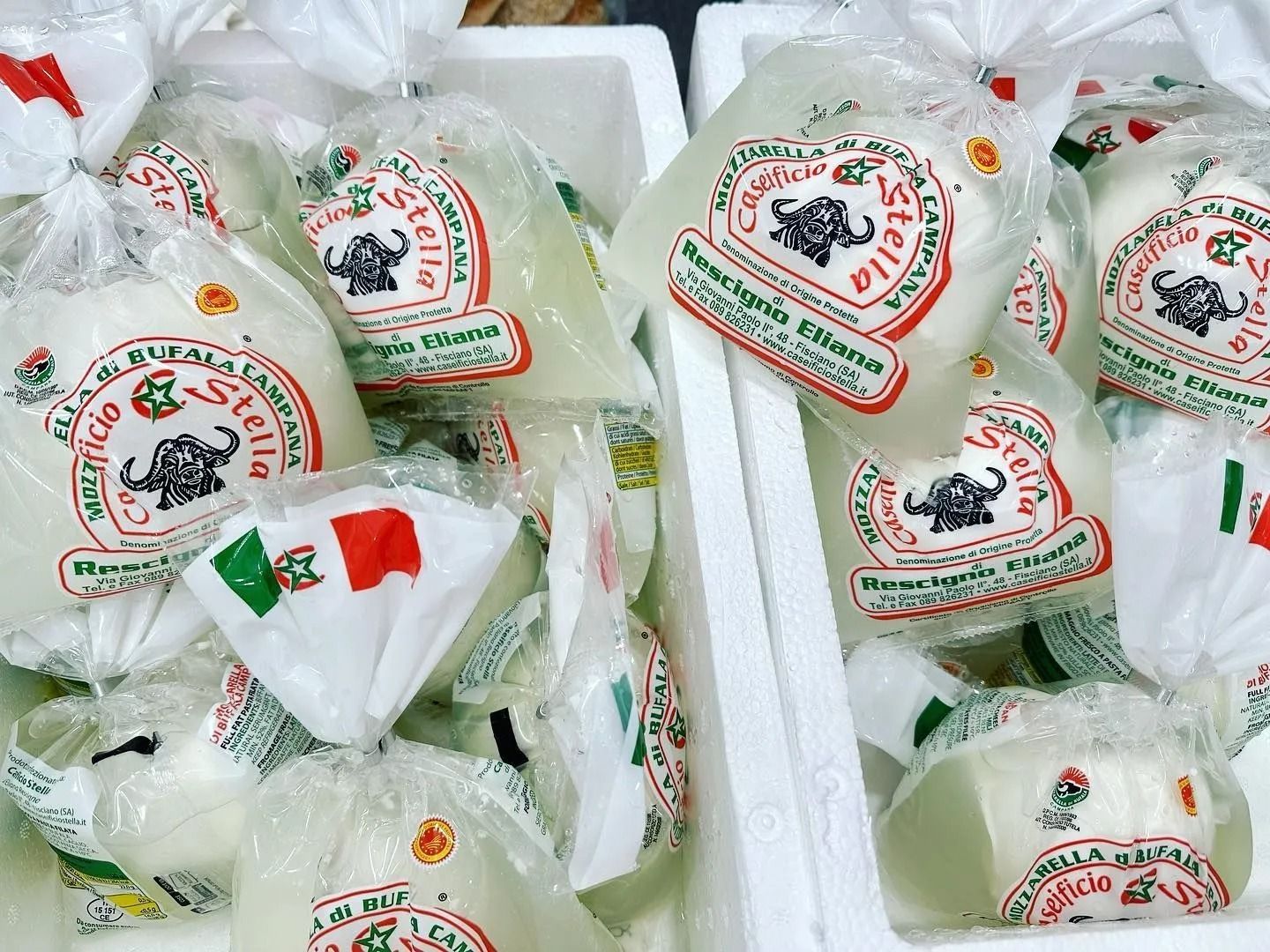 Bagged white cheese wheels with red-and-green labels stacked together in a market display