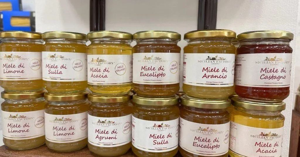 Rows of labeled homemade jam jars on a shelf, in assorted fruit flavors and gold lids