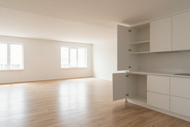 Bright empty living room with light wood floors, white walls, windows, and built-in shelving