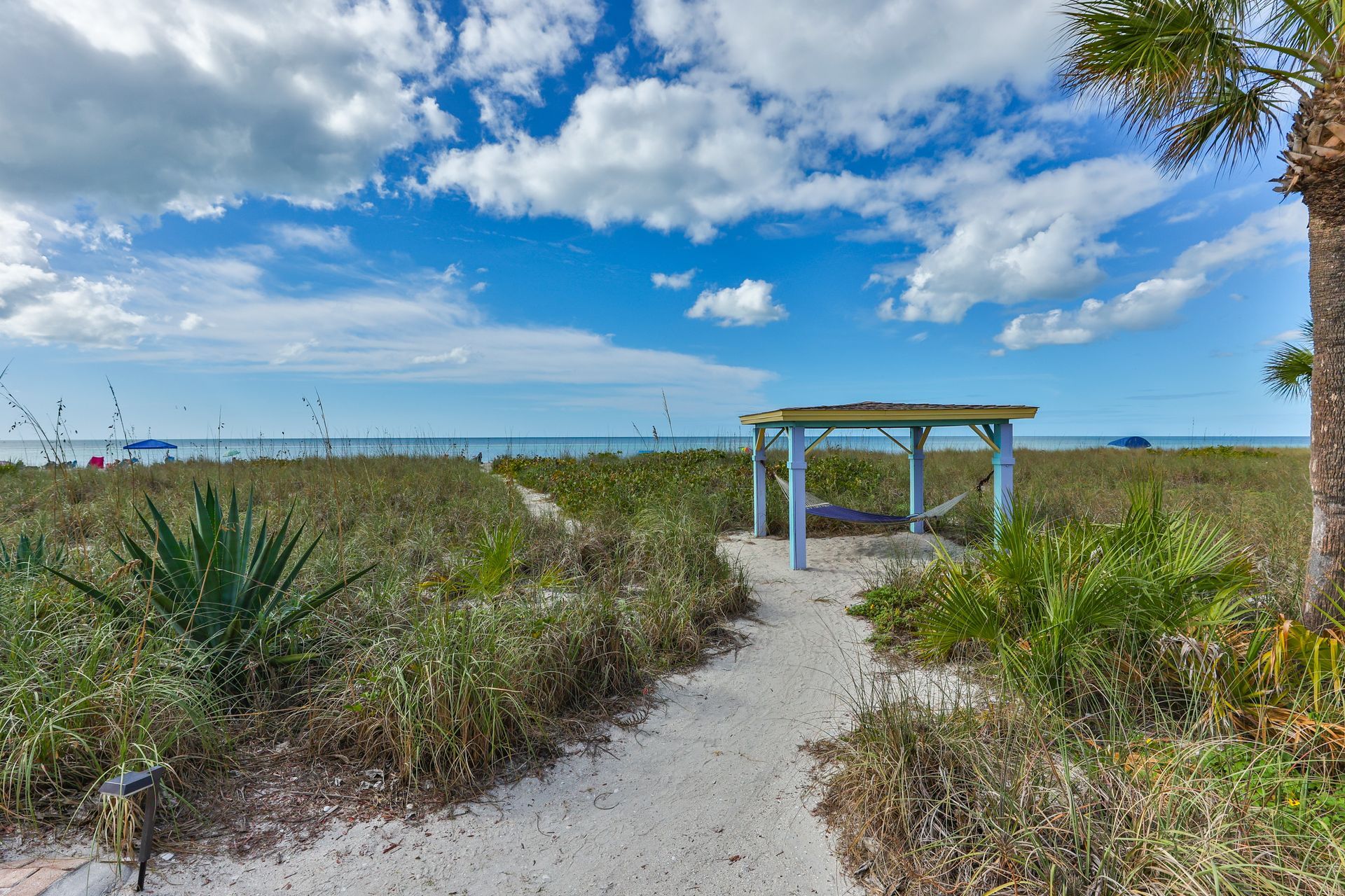 Sandy path leading to a beach gazebo, with ocean and blue sky in the background.
