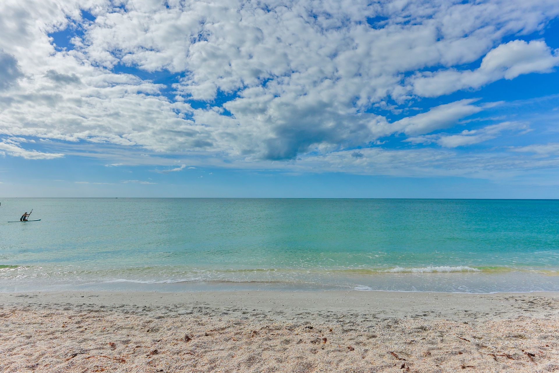 Beach scene: Blue ocean and sky with puffy white clouds, white sand.