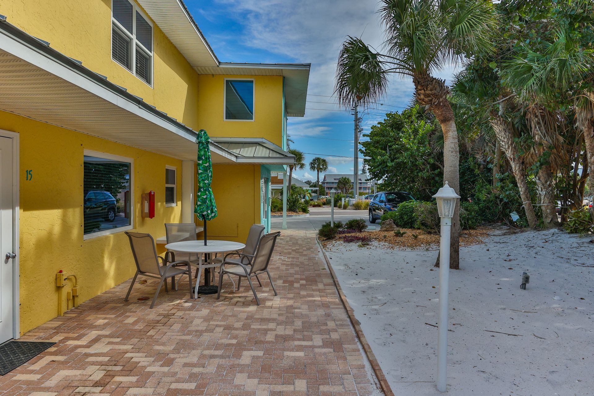 Yellow building with outdoor dining table, beach sand, and palm trees.