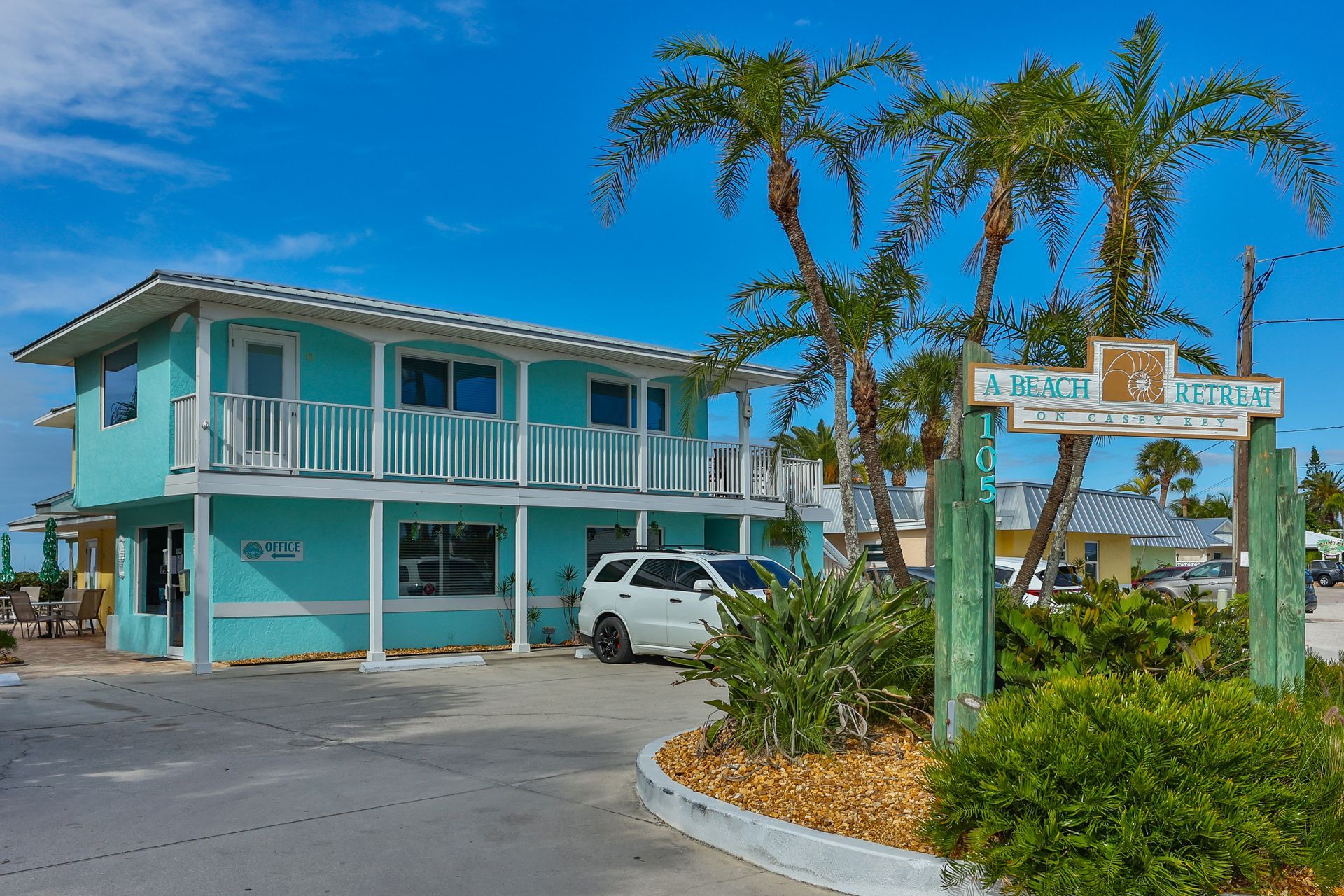 Turquoise two-story motel with white trim and balconies, palm trees, and sign for “A Fish Bungalows” on a sunny day.