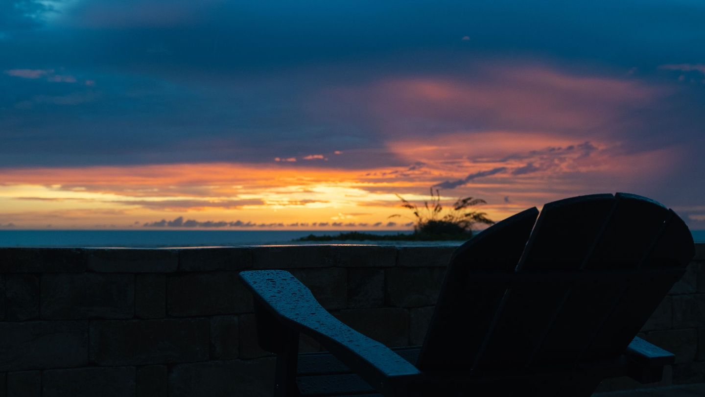 Silhouetted chair on a deck facing a colorful sunset over the ocean