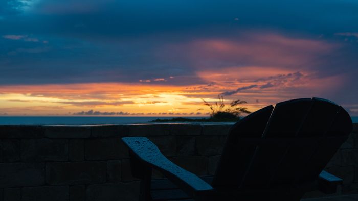 Silhouette of a patio chair against a sunset sky over a brick wall and distant horizon