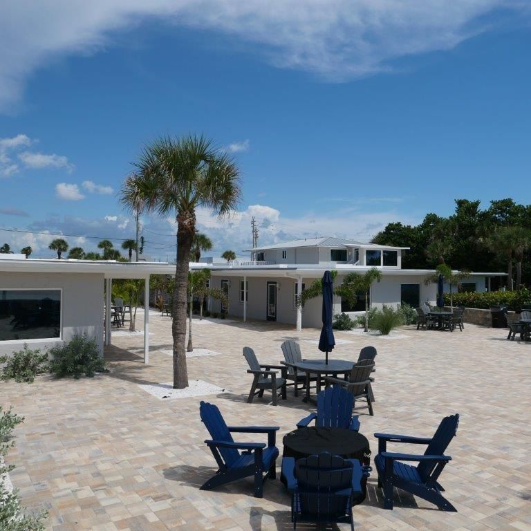Sunny resort patio with blue chairs, tables, palm tree, and white buildings under a clear sky