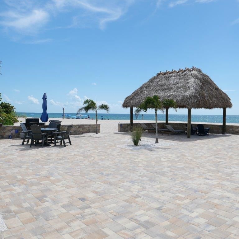 Beachfront patio with tables, blue umbrella, and thatched palapa overlooking the ocean under a clear sky