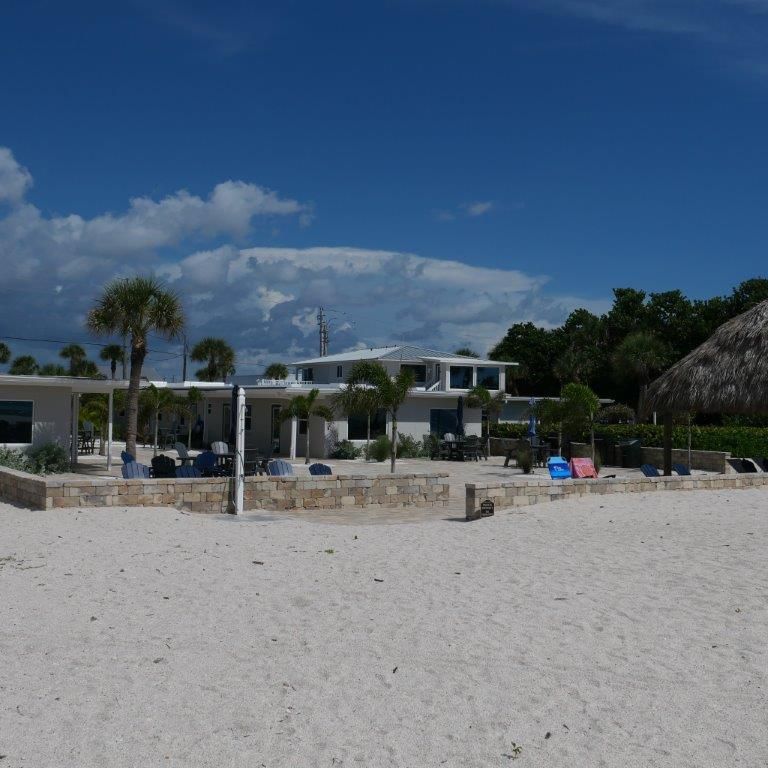 Sunny beach with white sand, palm trees, and a seaside villa under a blue sky